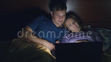 <strong>夫妻</strong>，男人和女人，在<strong>睡觉</strong>前在卧室的床上用笔记本电脑看电影。 看无聊的电影，摔倒